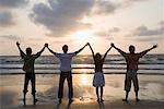 Rear view of three young men and a young woman standing side by side with holding hands on the beach