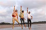 Three young men jumping with their hands raised on the beach