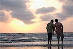 Rear view of two young men walking on the beach