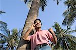 Low angle view of a young man leaning against a tree and talking on a mobile phone