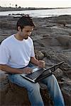 Vue grand angle d'un jeune homme travaillant sur un ordinateur portable à une côte, l'île Madh, Mumbai, Maharashtra, Inde