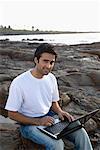 Portrait of a young man holding a laptop on his lap and smiling, Madh Island, Mumbai, Maharashtra, India