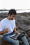 Young man working on a laptop on a coast, Madh Island, Mumbai, Maharashtra, India