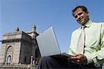 Portrait of a businessman using a laptop and smiling, Gateway of India, Mumbai, Maharashtra, India
