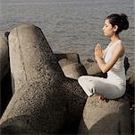 Profil de côté d'une jeune femme faisant du yoga sur une roche