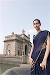 Porträt einer jungen Frau stehend mit einem Denkmal im Hintergrund, Gateway Of India, Mumbai, Maharashtra, Indien