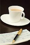 Close-up of a pen on a check book with a cup of tea on a saucer