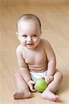 High angle view of a baby boy sitting on the hardwood floor and holding an apple