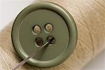 Close-up of a green button and a needle with a spool of thread