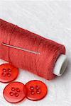 Close-up of red buttons and a needle with a spool of red thread