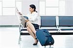 Businesswoman sitting on a chair at an airport and reading a newspaper