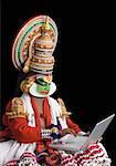 Close-up of a Kathakali dance performer sitting and using a laptop