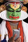 Close-up of a Kathakali dance performer holding a mobile phone