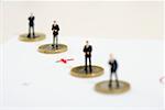 Plus sign between businessmen figurines standing on one Euro coins