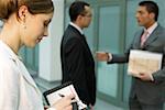 Two businessmen talking, in foreground businesswoman making notes