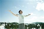 Young man standing in snowy mountain landscape with arms lifted, eyes closed