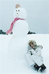 Teen girl leaning against snowman, sleeping