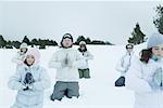 Groupe de jeunes amis à genoux dans la neige avec les mains jointes et les yeux fermés