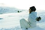 Jeune fille assise sur la neige, les yeux fermés et les bras tendus aux côtés