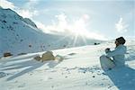 Teen girl sitting on snow in prayer position, sun shining over edge of mountain