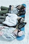 Three sisters lying on snow with heads resting on snowboard