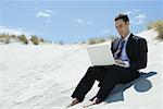 Businessman sitting on sand dune, using laZSop