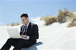 Businessman sitting on sand dune, using laZSop