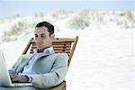 Businessman sitting in deck chair at beach, using laZSop