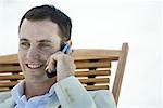 Businessman sitting in deck chair at beach, smiling