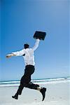 Businessman on beach, jumping into air with briefcase in hand