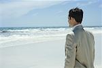 Businessman standing on beach, looking at ocean, waist up