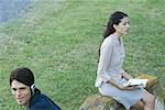 People sitting in park, man listening to headphones while woman reads book