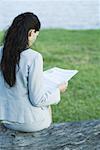 Businesswoman reading newspaper by lake, rear view