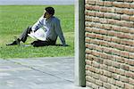 Homme d'affaires assis sur l'herbe avec laZSop et le journal, coin des briques au premier plan