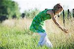 Young woman bending over to touch tall grass in rural field