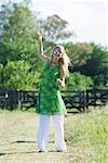 Young woman blowing bubbles in rural field, smiling at camera