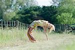 Young woman doing backbend in rural field