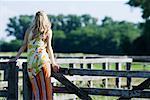 Young woman leaning against rural fence, rear view