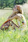 Young woman sitting in tall grass with knees up, holding head and looking up