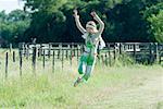 Young woman jumping in rural field with arms raised