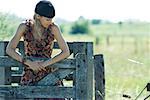 Young woman holding on to wooden fence, looking away