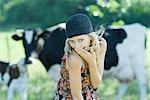 Young woman covering mouth with hand, looking at camera, cows in background