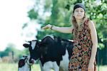 Young woman standing in front of cows, arm outstretched behind her, smiling at camera