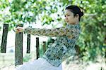 Young woman holding on to rural fence, leaning back