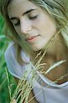 Young woman holding tall grass, eyes closed, close-up