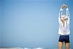 Young woman in active wear stretching on beach, rear view