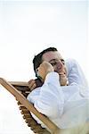 Young man sitting in deck chair, using cell phone