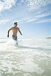 Young man running through surf on beach