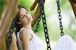 Young woman sitting on swing with knee up, looking away