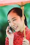 Young woman wearing traditional Chinese clothing, holding parasol and using cell phone